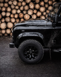 Land Rover Defender 110 Black Design Edition frontside in front of wood